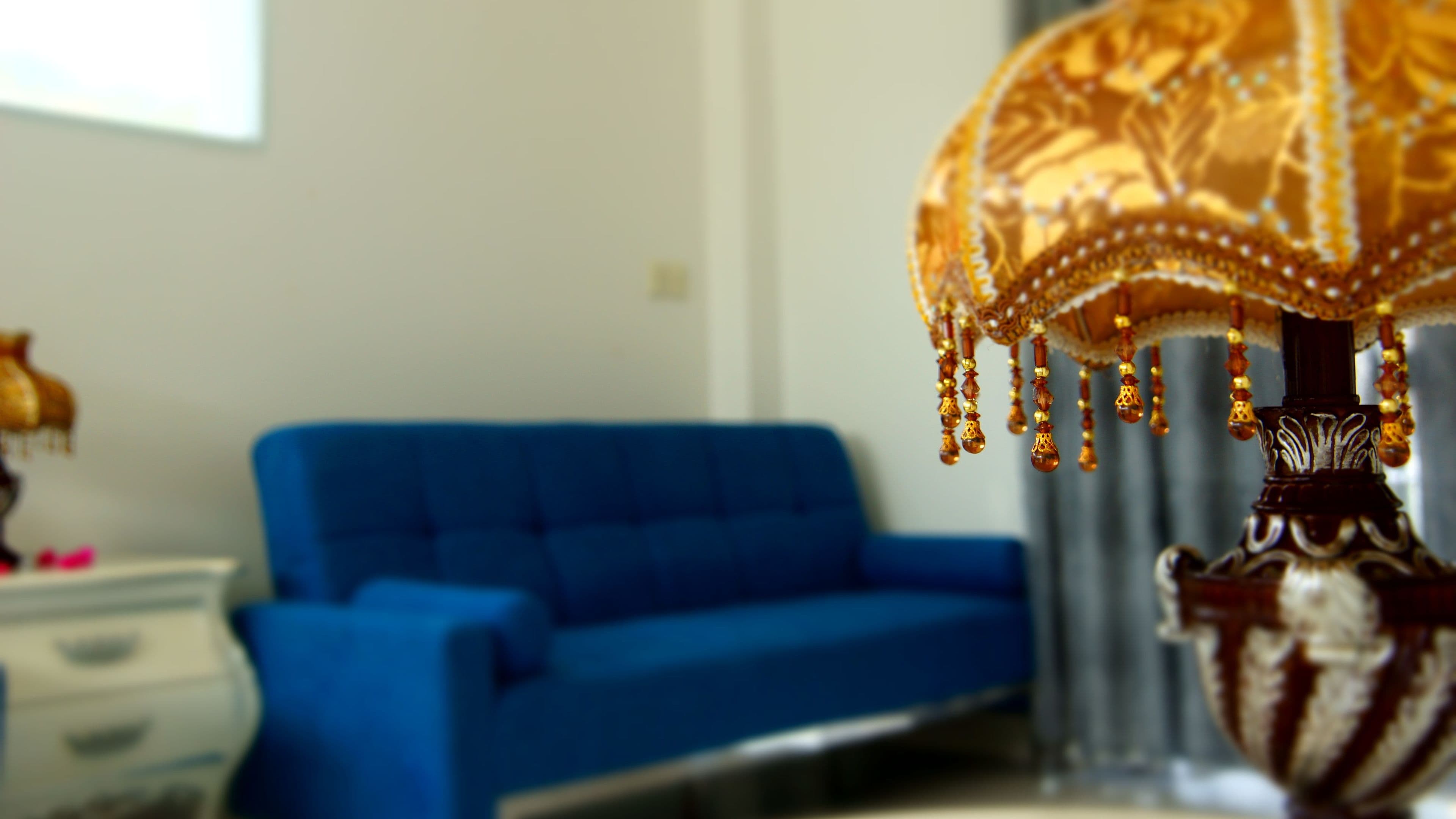 A room with a blue sofa, a lamp with a decorative shade, and a dresser.