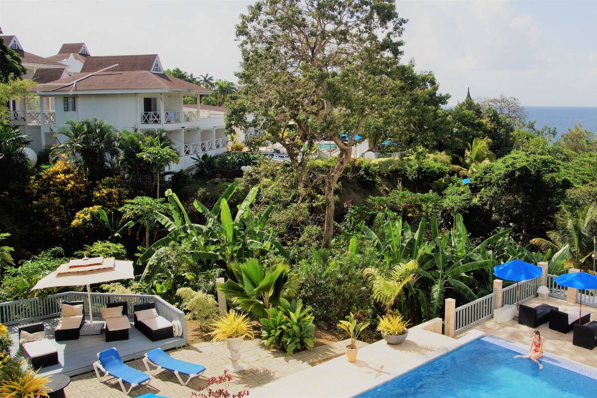 A poolside area with lounge chairs, umbrellas, and a view of the sea.