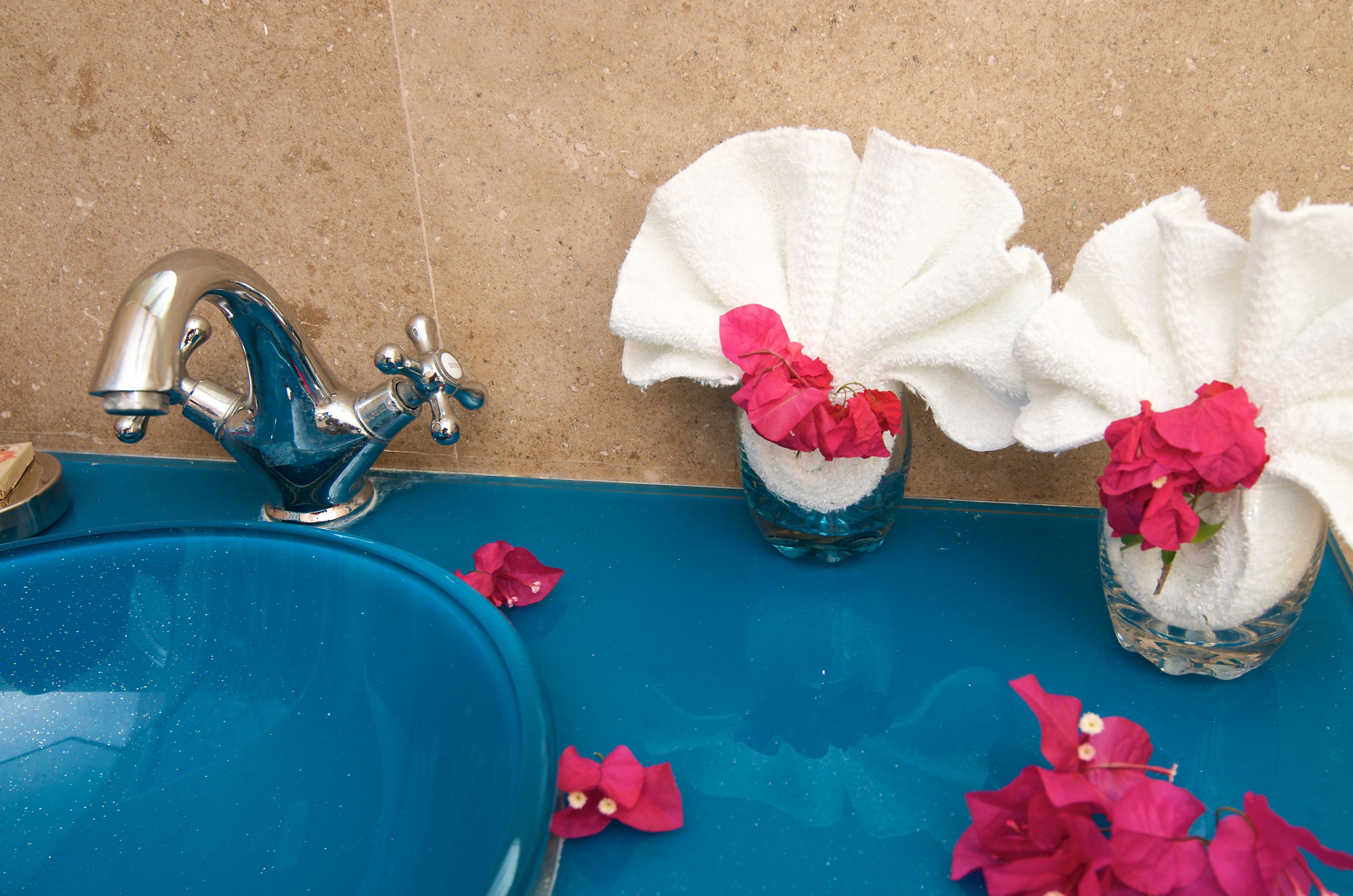 A bathroom with a blue sink, a silver faucet, and two glass containers with white towels and pink flowers.