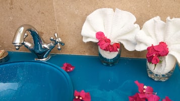 A bathroom with a blue sink, a silver faucet, and two glass containers with white towels and pink flowers.