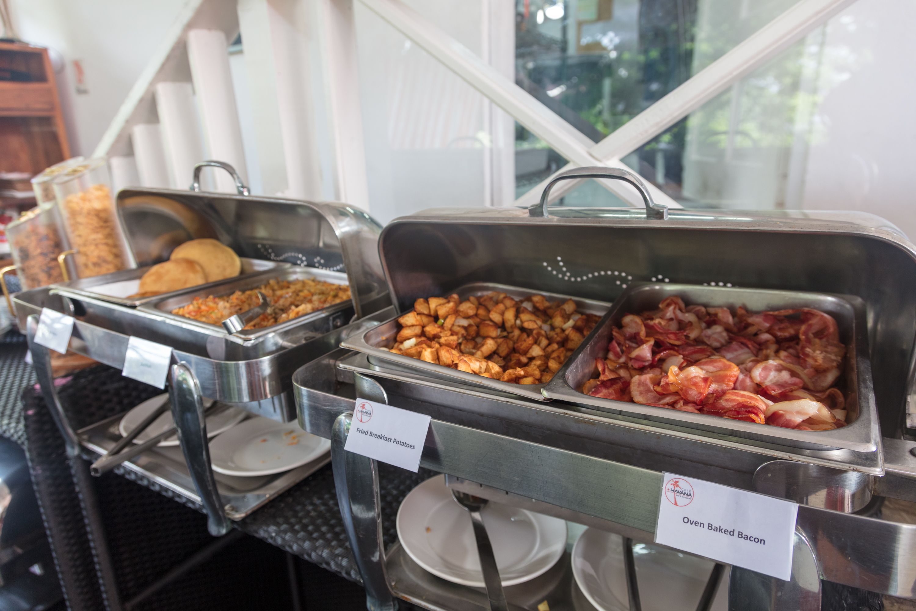 A buffet with labeled food options including fried breakfast potatoes and oven-baked bacon.
