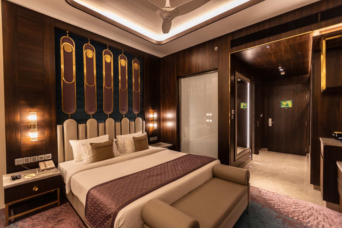 Una habitación de hotel con una cama grande, mesitas de noche, un espejo y una puerta que da a un baño.
