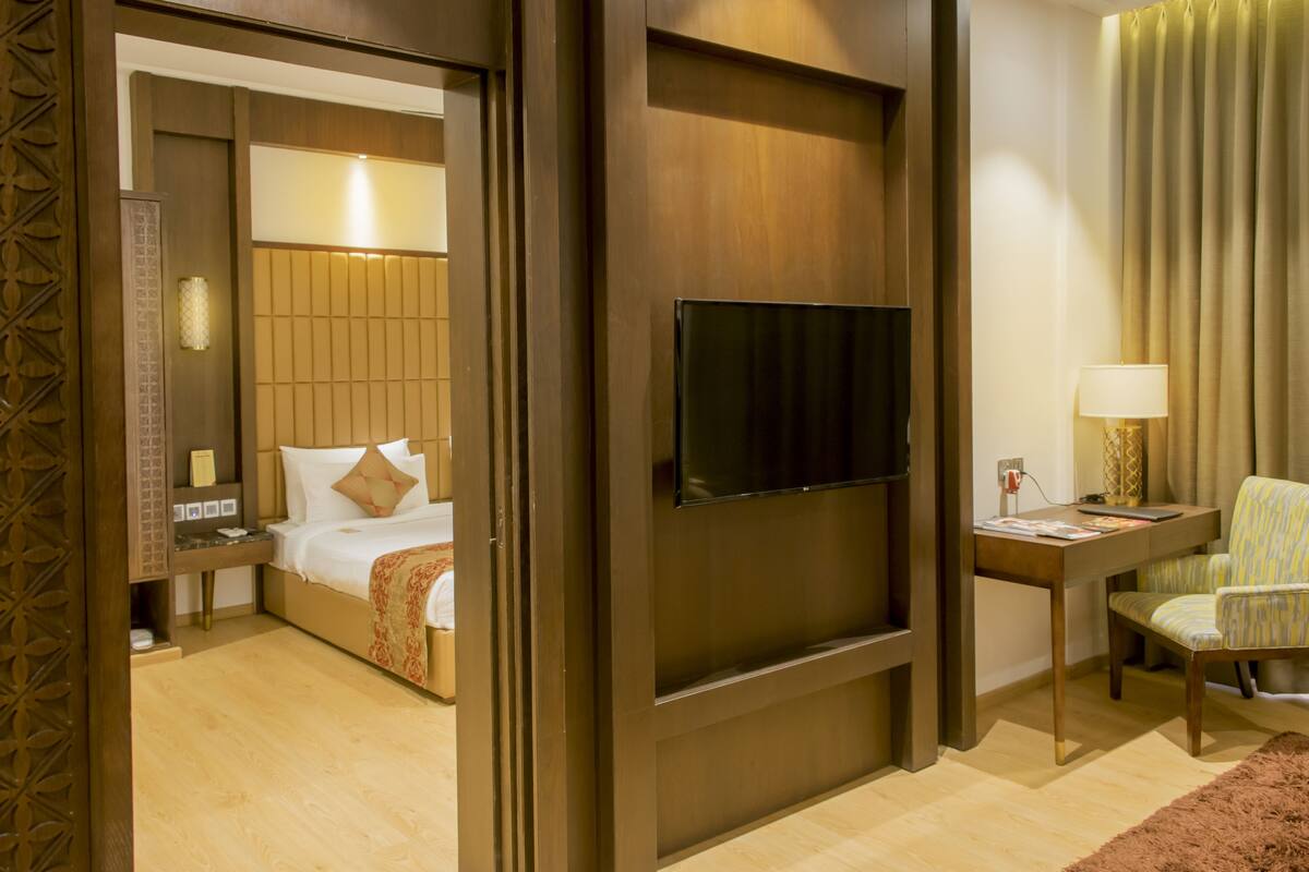 Habitación de hotel con cama, televisor montado en la pared, escritorio con lámpara y una silla.