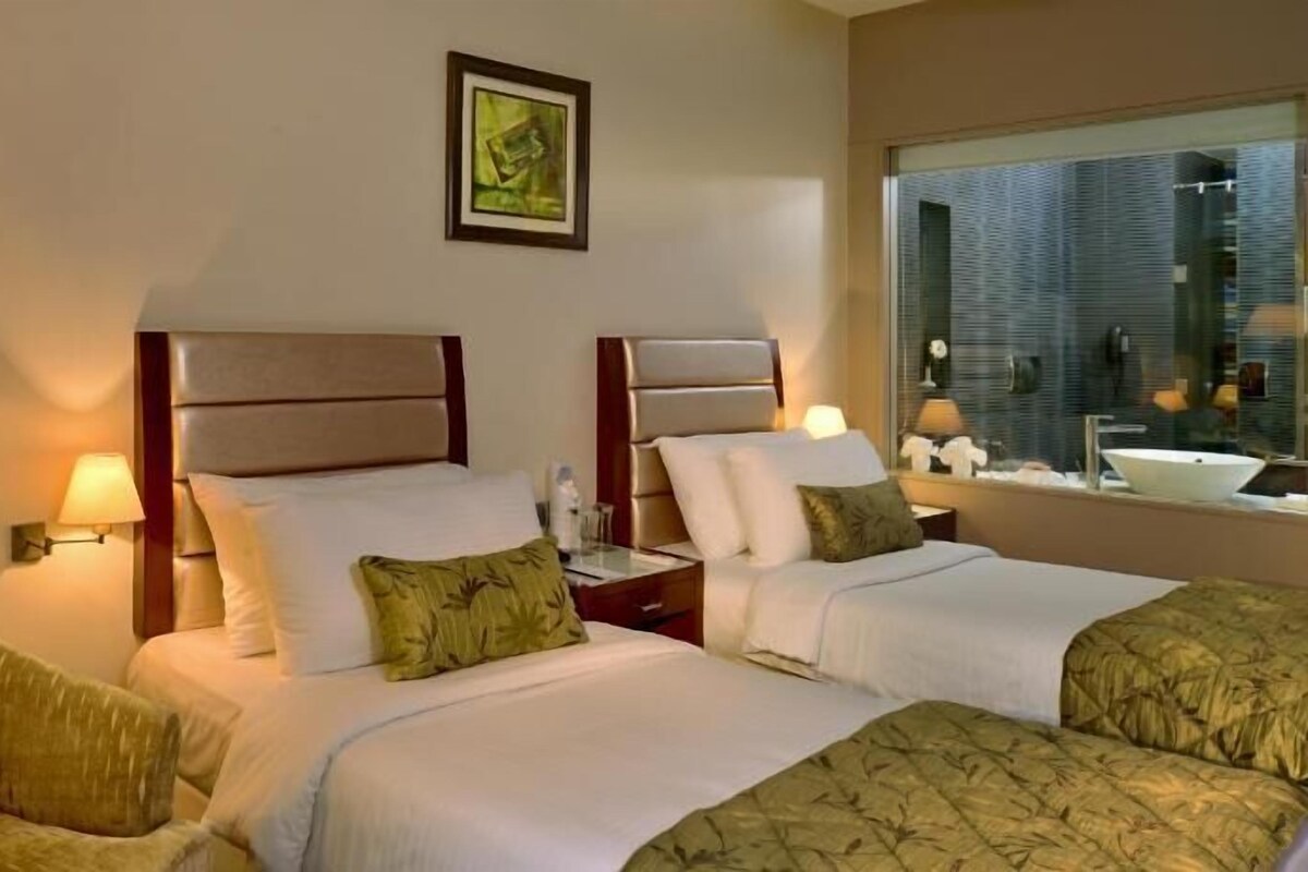 Habitación de hotel con dos camas, una silla, una mesita de noche, una lámpara y una ventana con vistas.