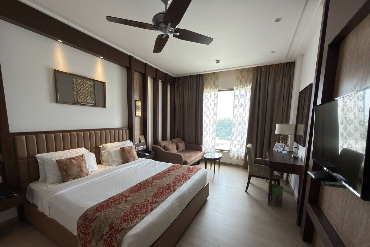 Habitación de hotel con una cama grande, un sofá, un escritorio con televisor y un ventilador de techo.
