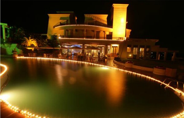 A nighttime view of a hotel with a pool, outdoor seating, and a well-lit facade. - The Corinthians Resort (Pune)