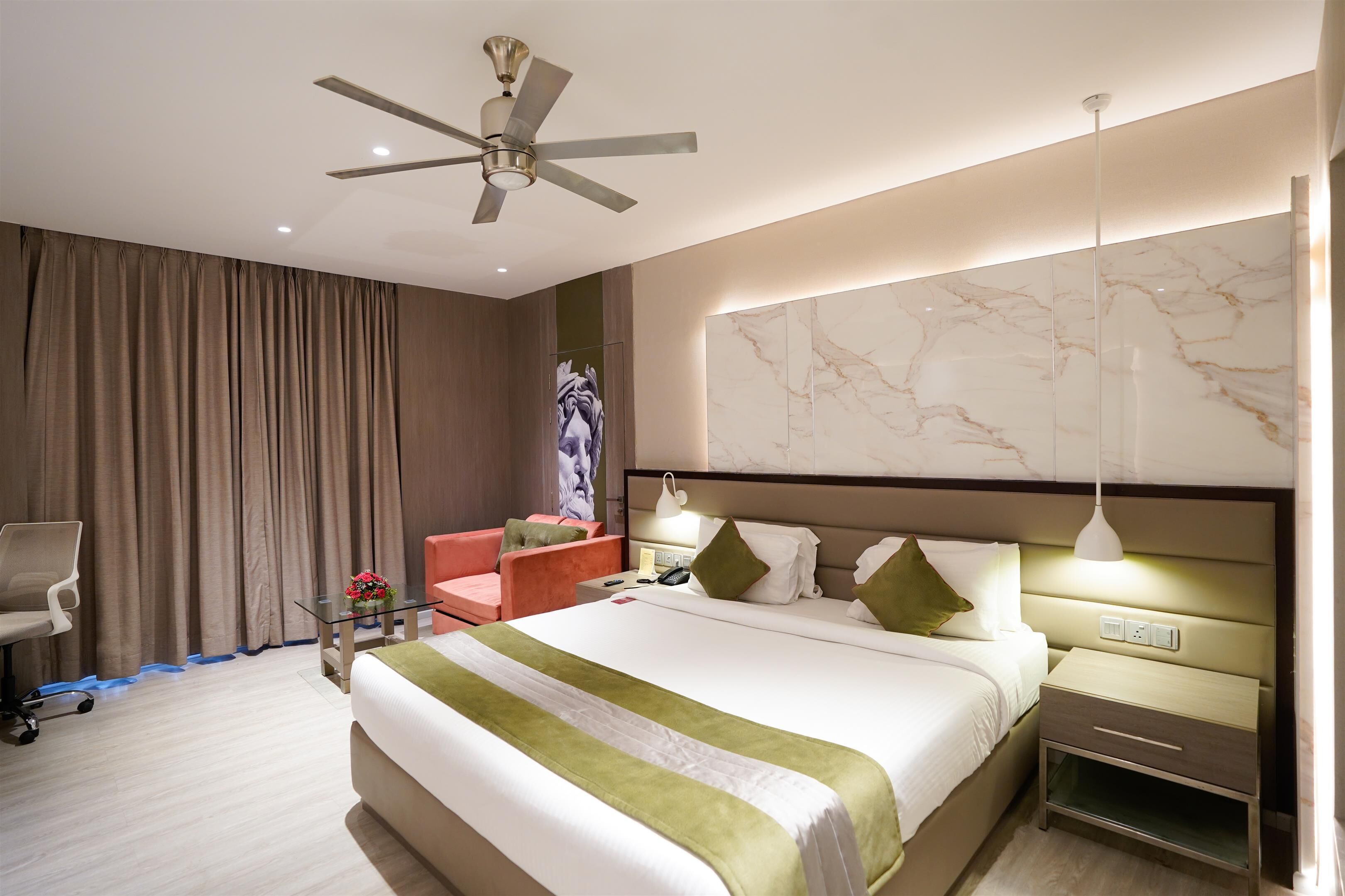 A modern hotel room with a large bed, a desk, a chair, a ceiling fan, and a marble wall.