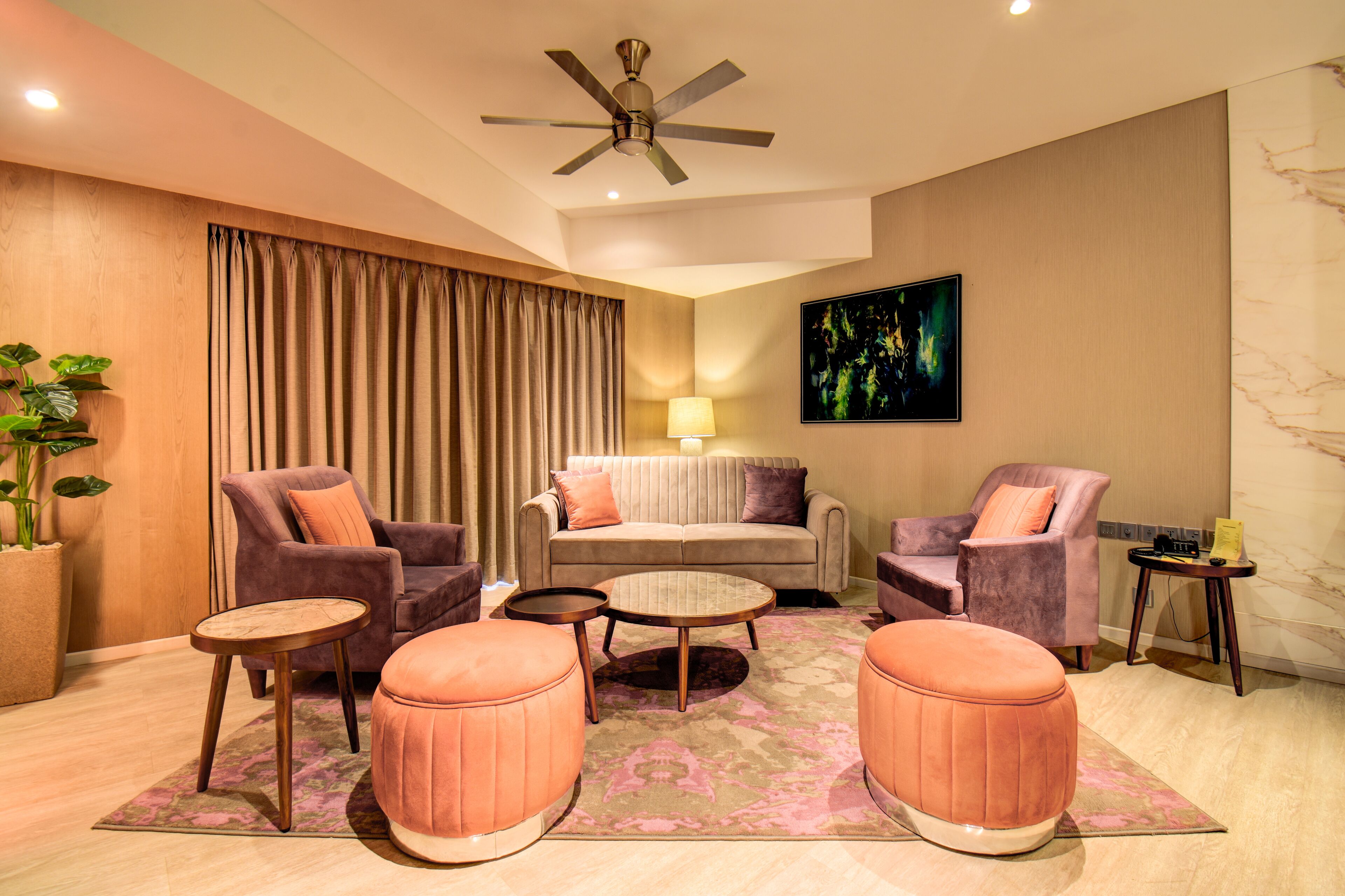 A modern living room with a ceiling fan, a sofa, two armchairs, a coffee table, and ottomans.