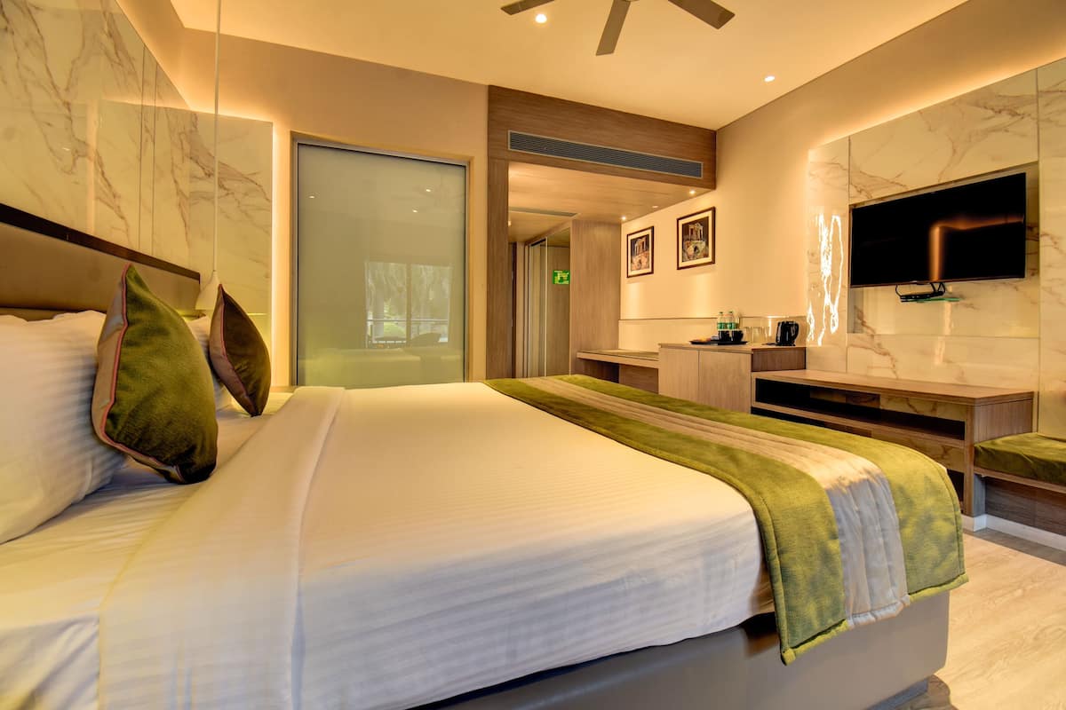 Habitación de hotel moderna con una cama grande, un televisor montado en la pared y un baño visible a través de una puerta de cristal.
