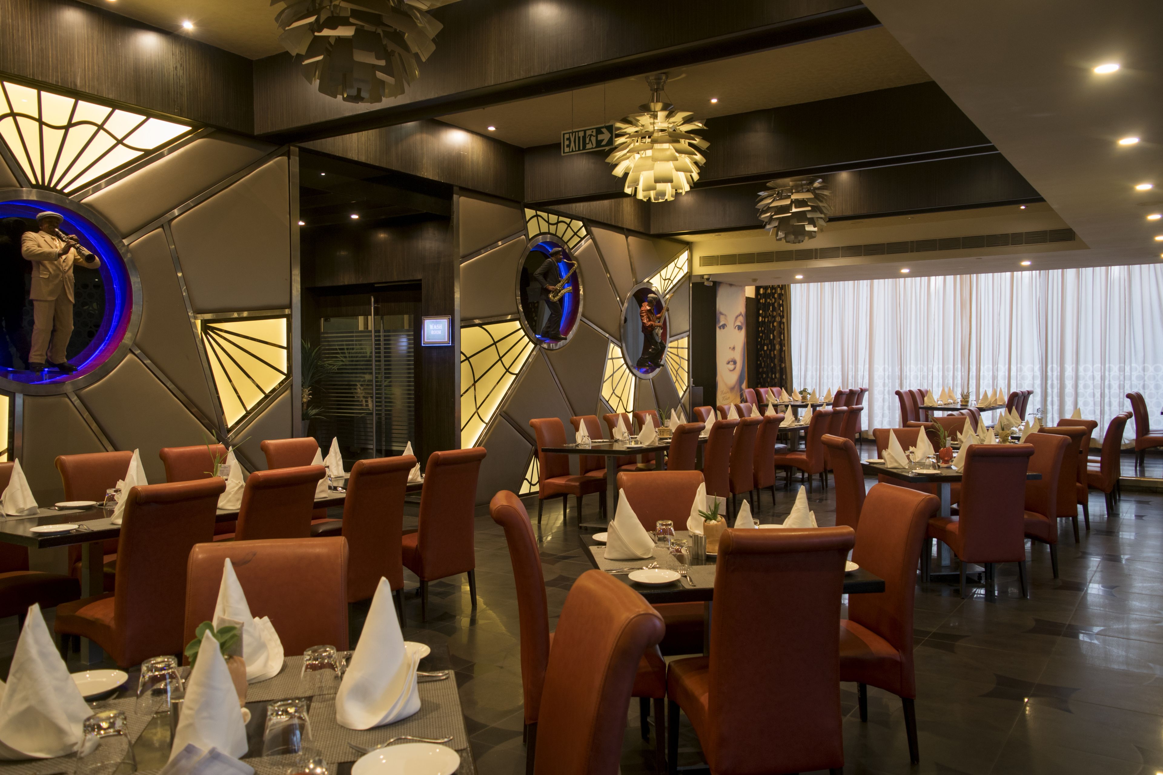 Un restaurante moderno con sillas tapizadas en rojo, mesas redondas y un techo decorativo.