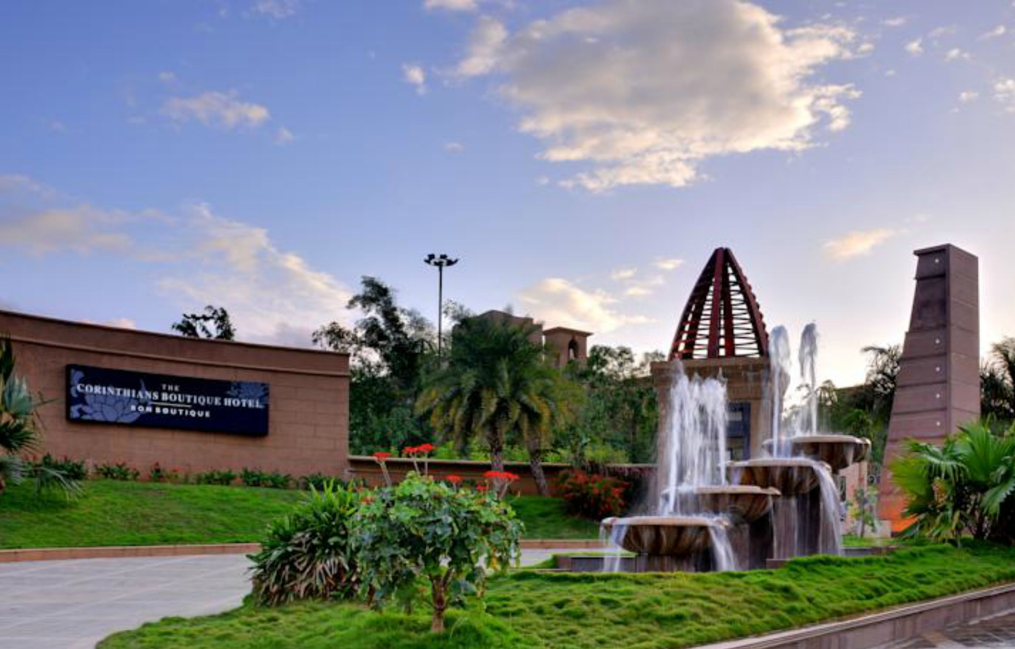 The Corinthians Boutique Hotel with a landscaped garden, a water feature, and a distinctive tower structure.