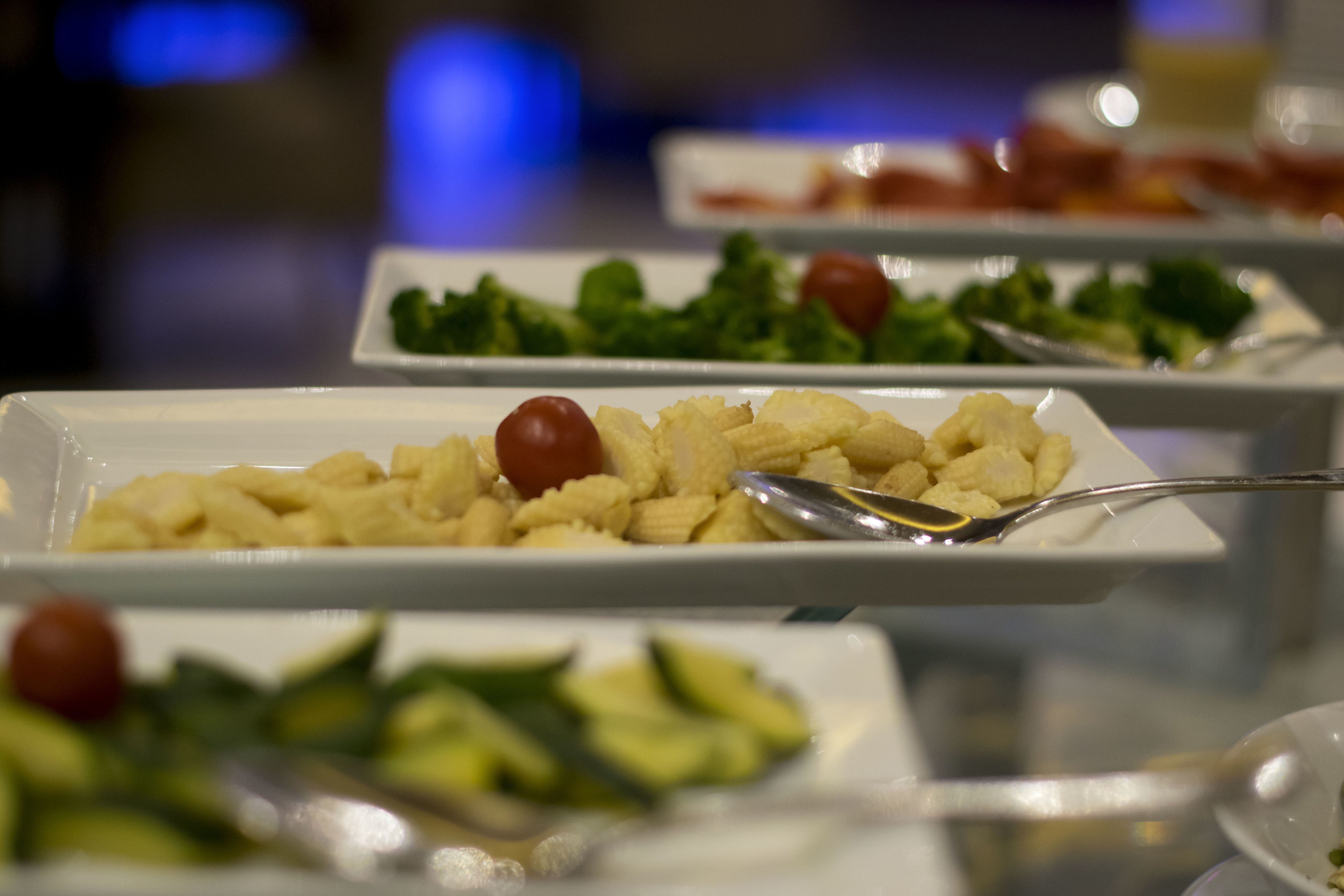 A buffet with various dishes including pasta, vegetables, and a small bowl of sauce.