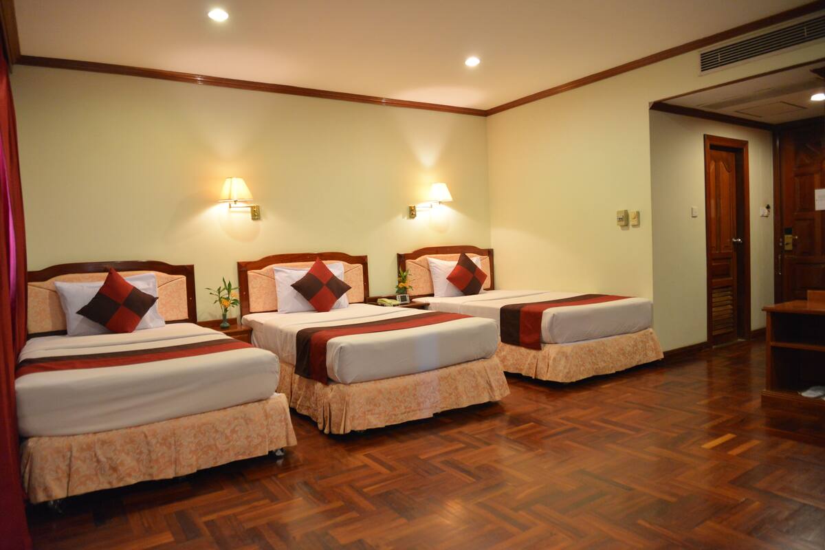 Habitación de hotel con tres camas, suelo de madera y lámparas fijadas a la pared.