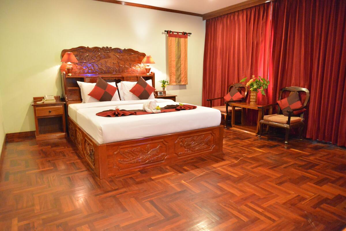 Habitación de hotel con una cama de madera, una mesita de noche, una silla y una cortina roja.