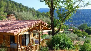 A wooden cabin with a tiled roof, surrounded by greenery and hills. - Lagrange Vacances Les Cottages Varois (Sollies-Toucas)