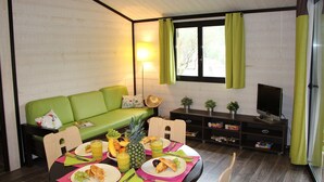 A compact living space with a green sofa, a dining table set with food and drinks, a television, and a small bookshelf. - Lagrange Vacances Les Cottages Varois (Sollies-Toucas)
