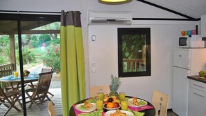 A dining area with a table set for breakfast, a window with a view of greenery, and a kitchen area with a microwave. - Lagrange Vacances Les Cottages Varois (Sollies-Toucas)