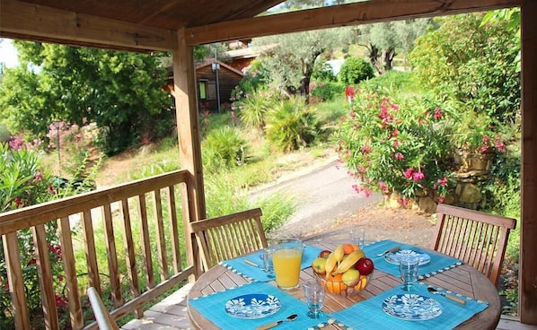 Una terraza de madera con una mesa dispuesta para dos, con manteles azules y un frutero.