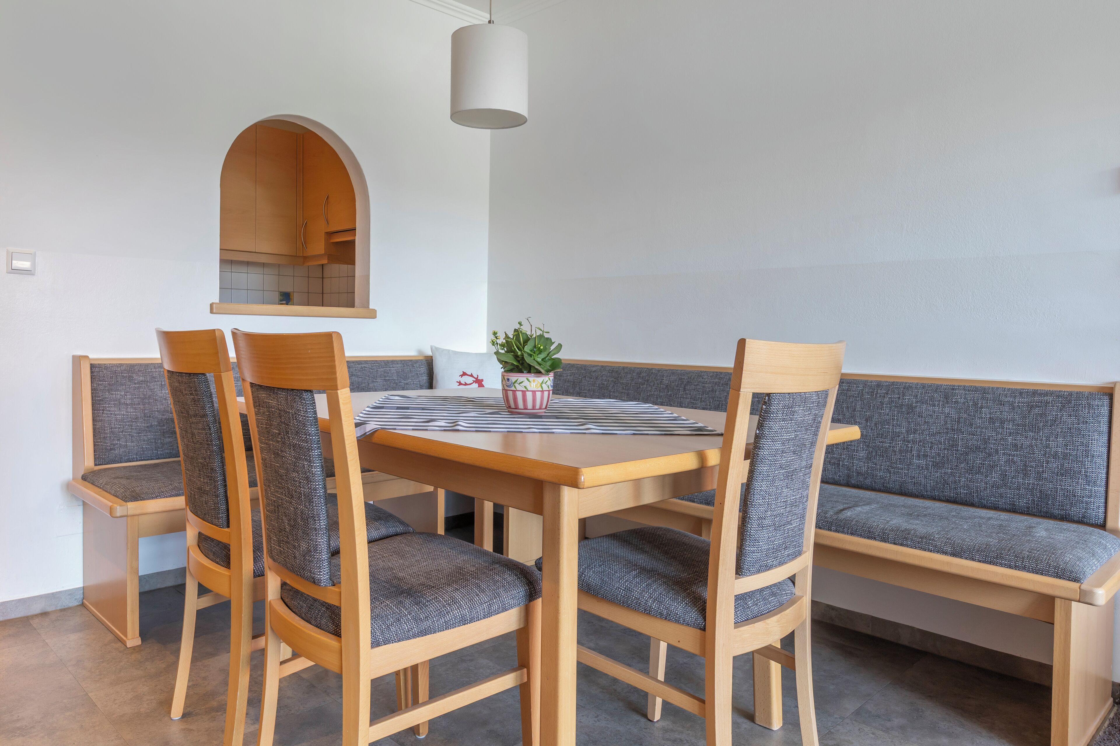 A dining area with a wooden table, four chairs, a bench, and a hanging light fixture.