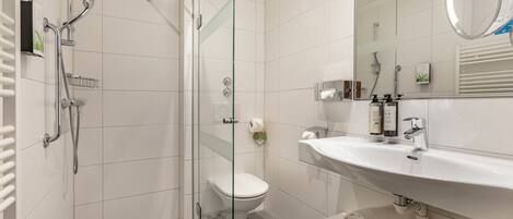 A modern bathroom with a glass-enclosed shower, a white toilet, a large sink with a mirror, and neatly rolled towels.
