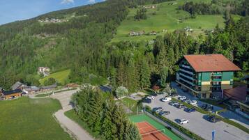A hotel with a tennis court, surrounded by greenery and a mountainous backdrop.