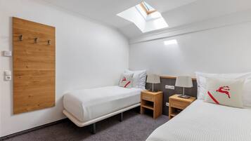 Habitación de hotel con dos camas individuales, un panel de madera en la pared, un tragaluz y una mesita de noche de madera con una lámpara.