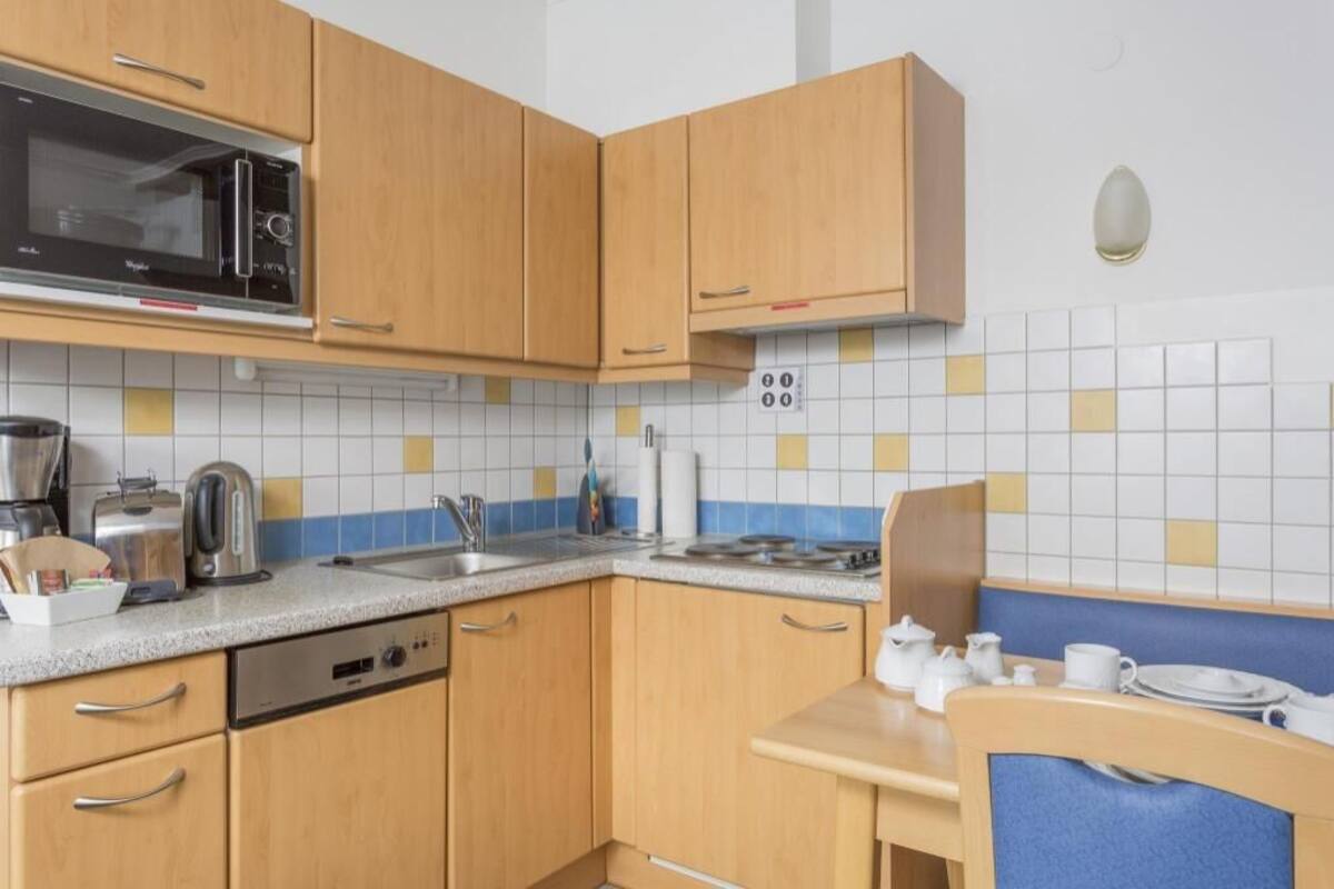A compact kitchen with wooden cabinets, a microwave, a kettle, a toaster, and a dishwasher.