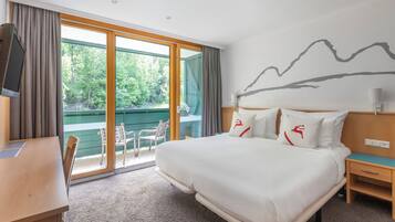 A hotel room with a large bed, a desk, and a view of greenery through the sliding glass door.