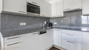 A modern kitchen with white cabinets, granite countertops, a built-in oven, and a dishwasher.