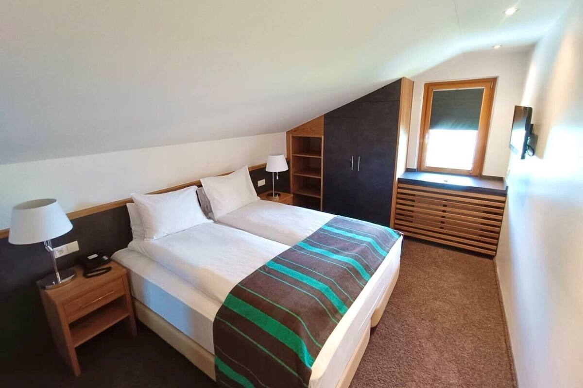A bedroom with a bed, nightstands, a dresser, and a window.