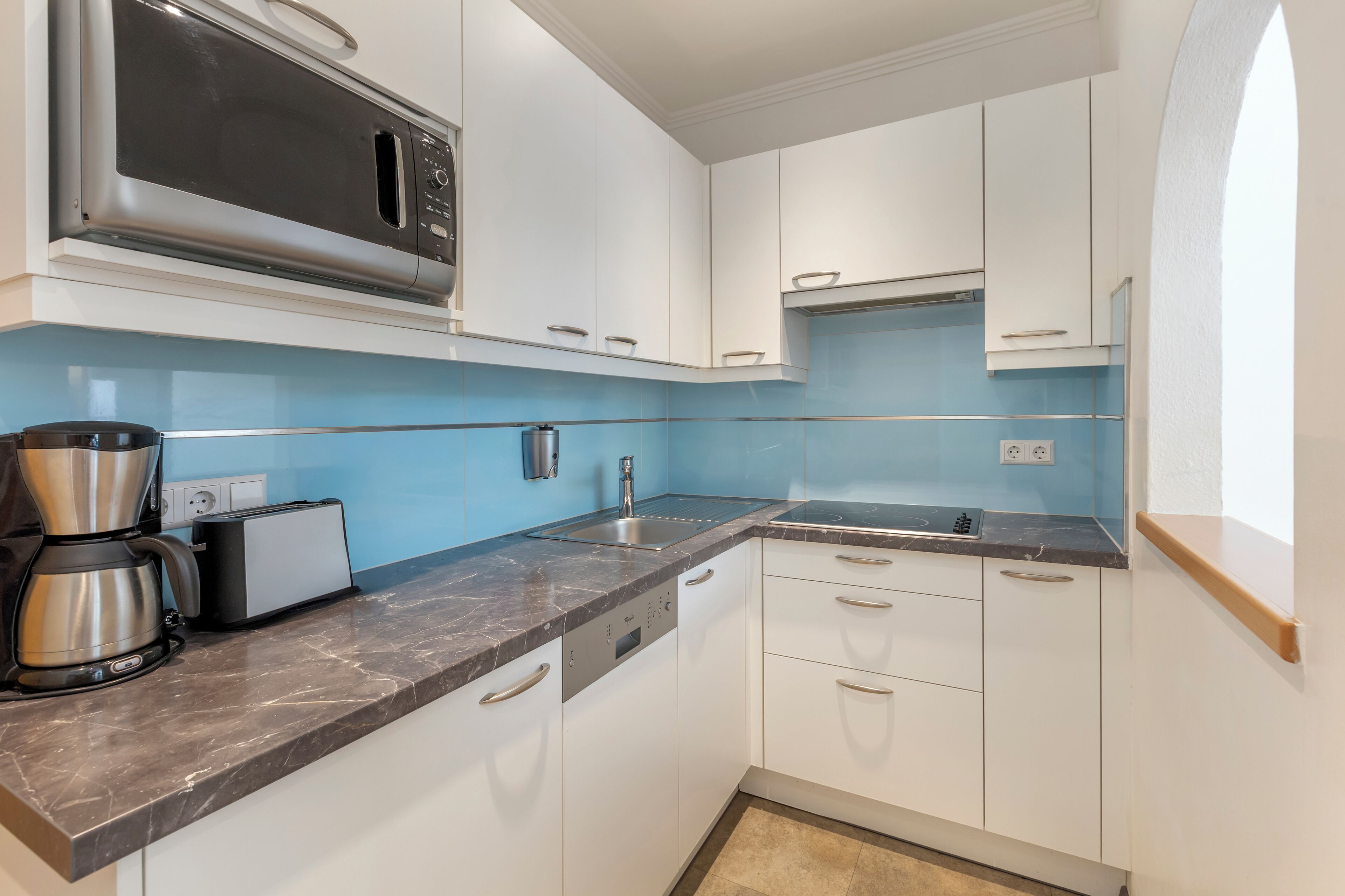 A modern kitchen with white cabinets, a black countertop, and a built-in microwave.
