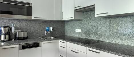 A modern kitchen with white cabinets, granite countertops, a built-in oven, a coffee maker, and a toaster.