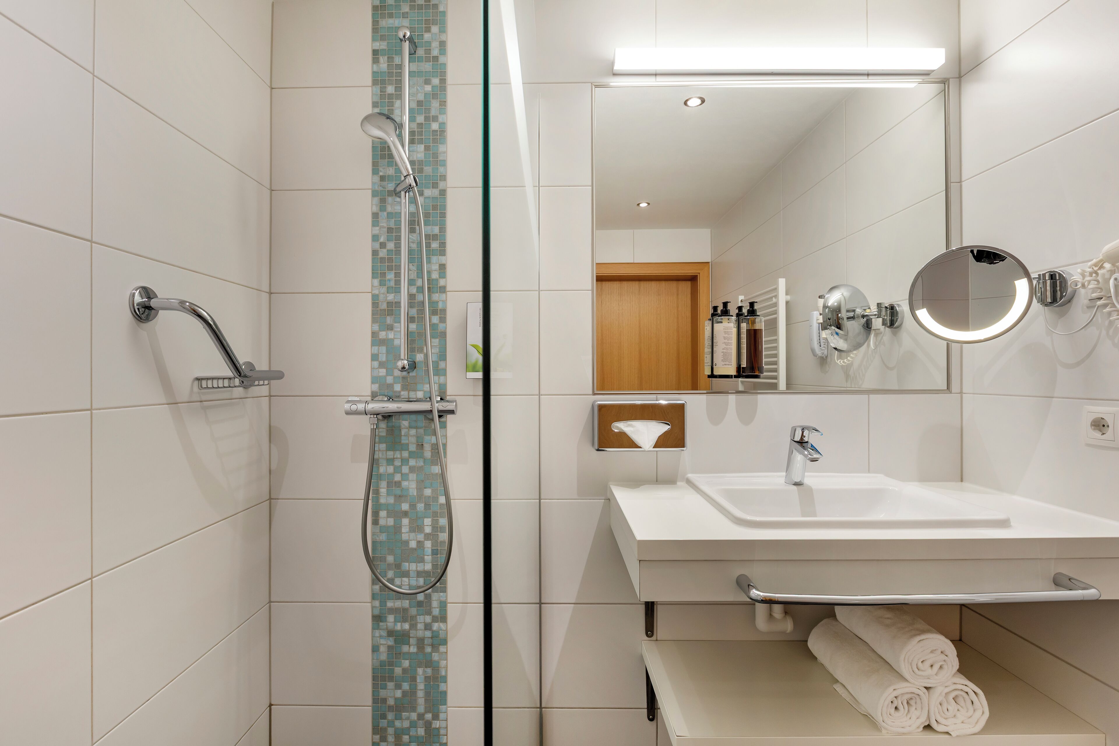 A modern bathroom with a glass shower enclosure, a white sink, and a mirror.