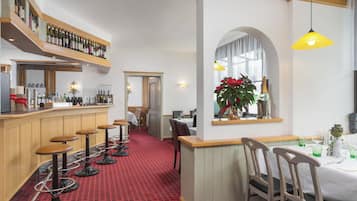 A restaurant with a red carpet, wooden bar, and multiple stools.