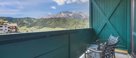 Een balkon met uitzicht op bergen, een groene wand en twee stoelen.
