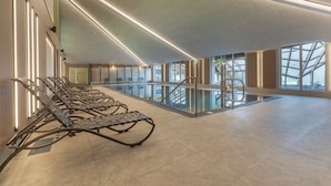 A modern indoor space with a long row of metal loungers, a glass railing, and a staircase leading to an upper level. - Alpine Club (Schladming)