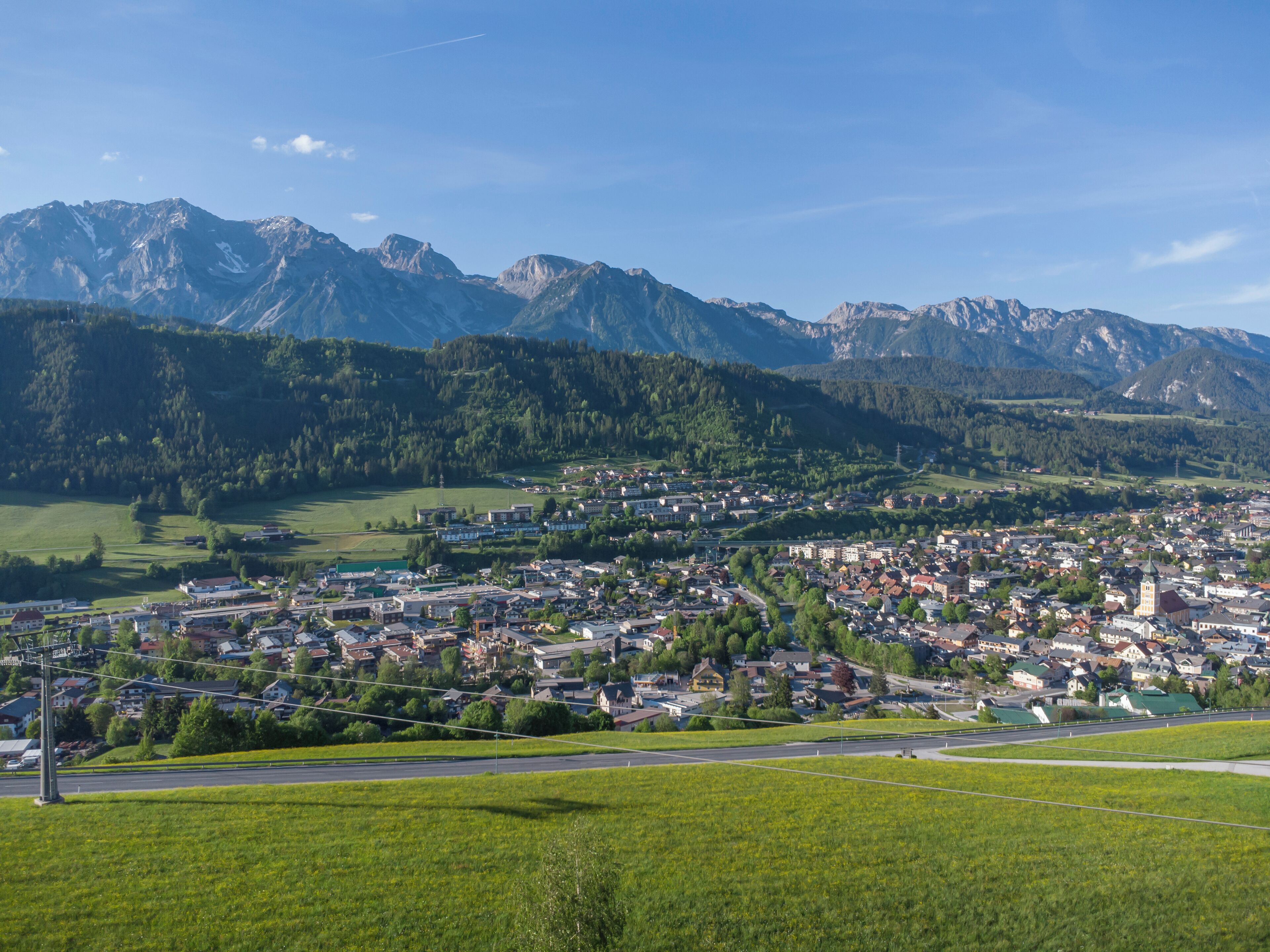 A town with a central square, surrounded by residential buildings and a mountain range in the background.