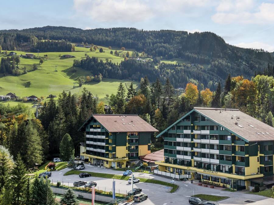 A hotel with a green and yellow facade, multiple floors, and a parking area.