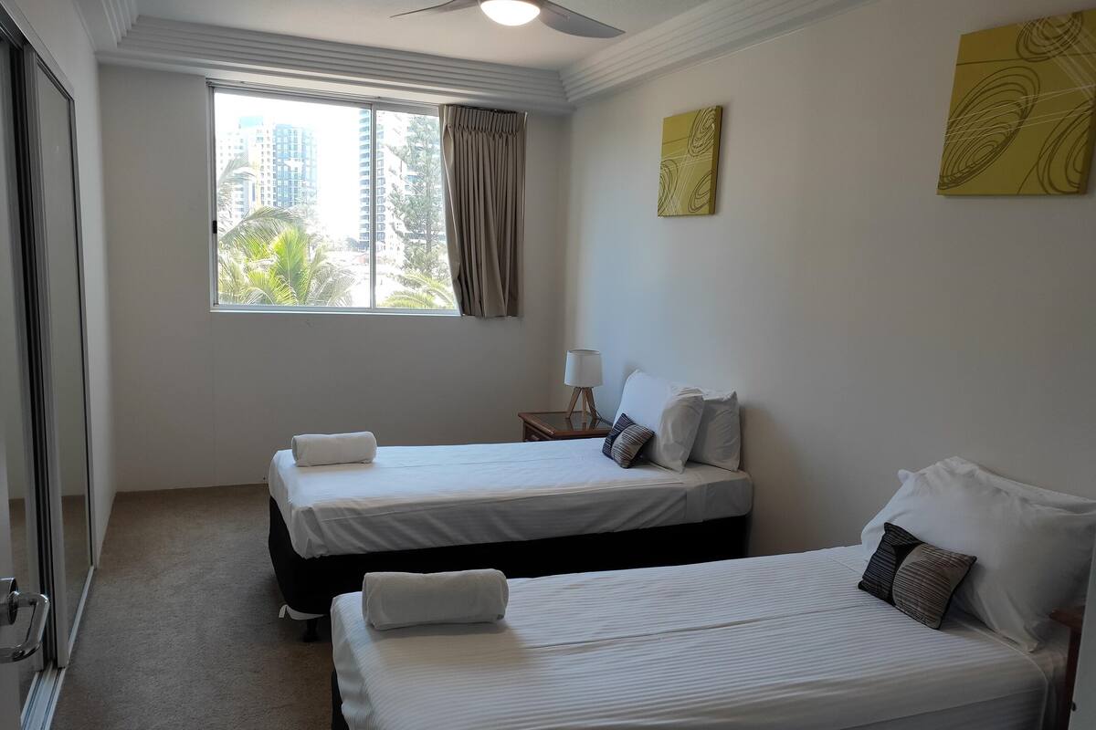 A hotel room with two beds, a ceiling fan, a window with curtains, and artwork on the walls.