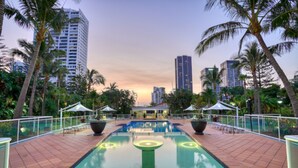 Una piscina con sillas de descanso y sombrillas, rodeada de palmeras y edificios altos.