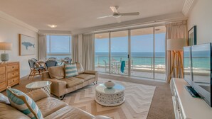 Un salón amplio con un ventanal grande con vistas a la playa, un ventilador de techo y un televisor de pantalla plana.