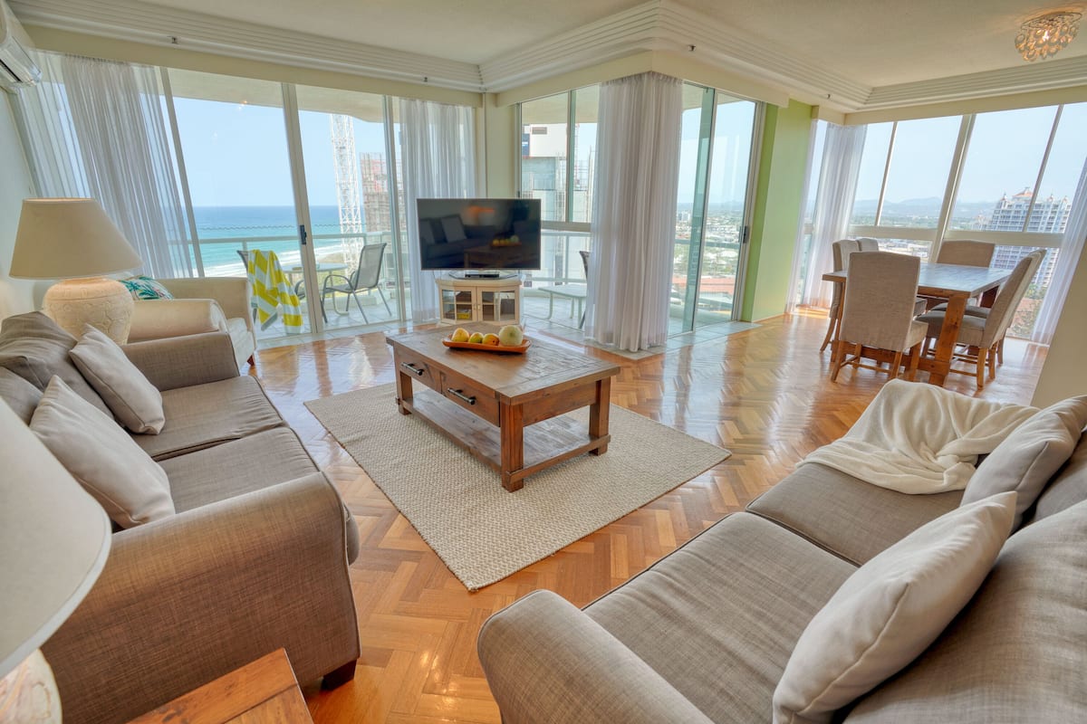 A spacious living room with a large TV, comfortable seating, and a view of the ocean.