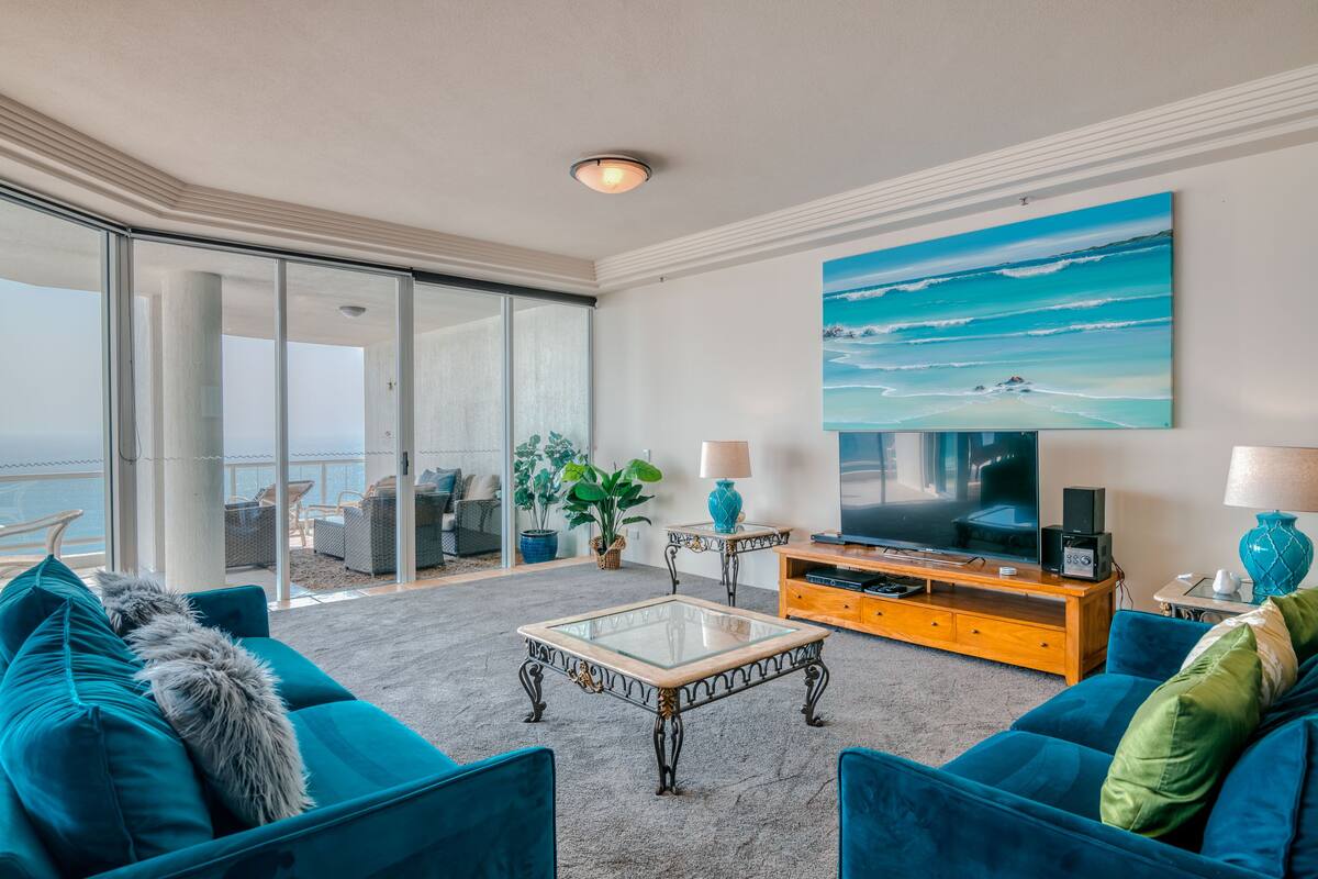 A spacious living room with a large TV, comfortable seating, and a view of the ocean.