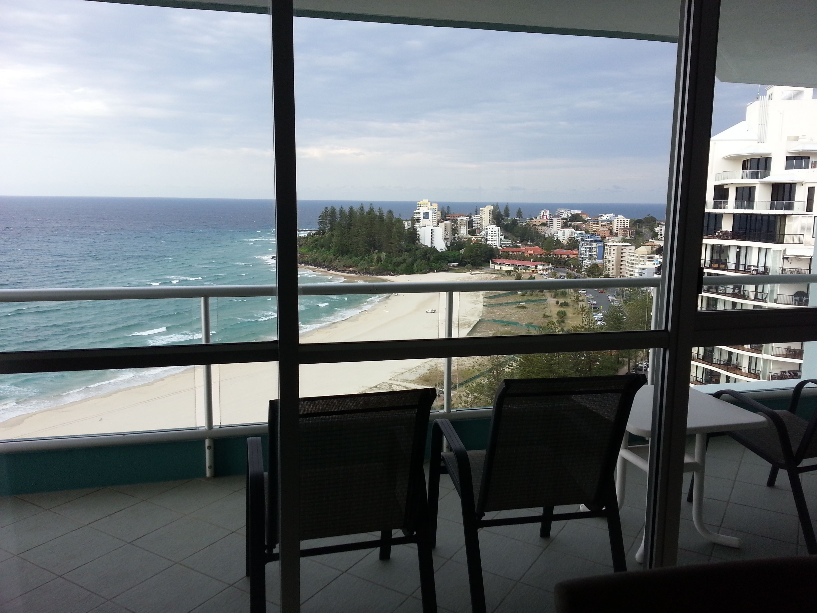 Un balcon avec vue sur l’océan et une plage, comprenant deux chaises et une table.