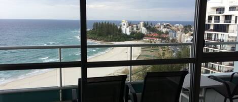 Un balcon avec vue sur l’océan et une plage, comprenant deux chaises et une table.