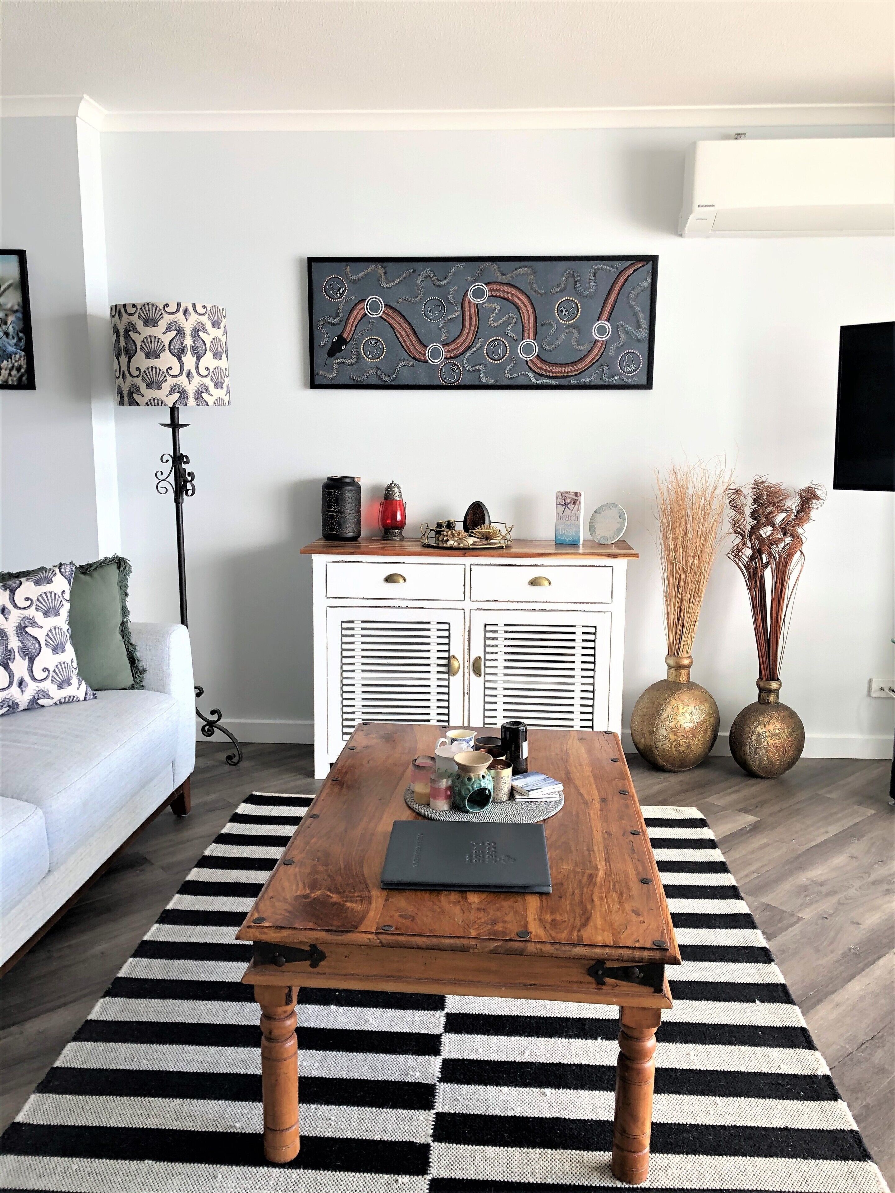 Ein Wohnzimmer mit Couchtisch aus Holz, weißem Sofa, dekorativen Lampen und einem an der Wand hängenden abstrakten Gemälde.