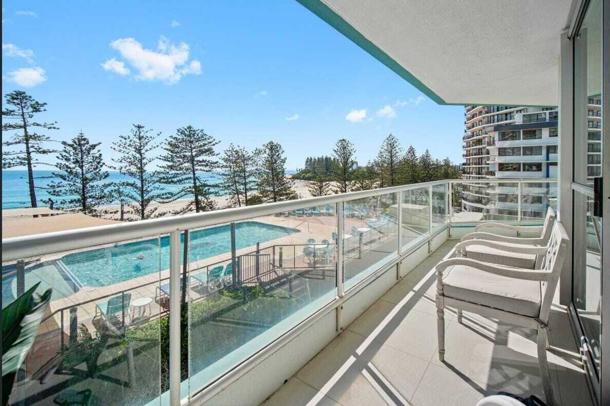 A balcony with a glass railing overlooking a swimming pool and beach.