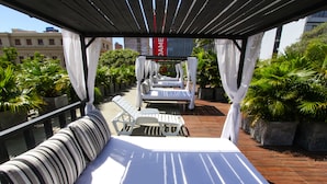 Terraza en la azotea con toldo, dos camas, un sofá y plantas en macetas.