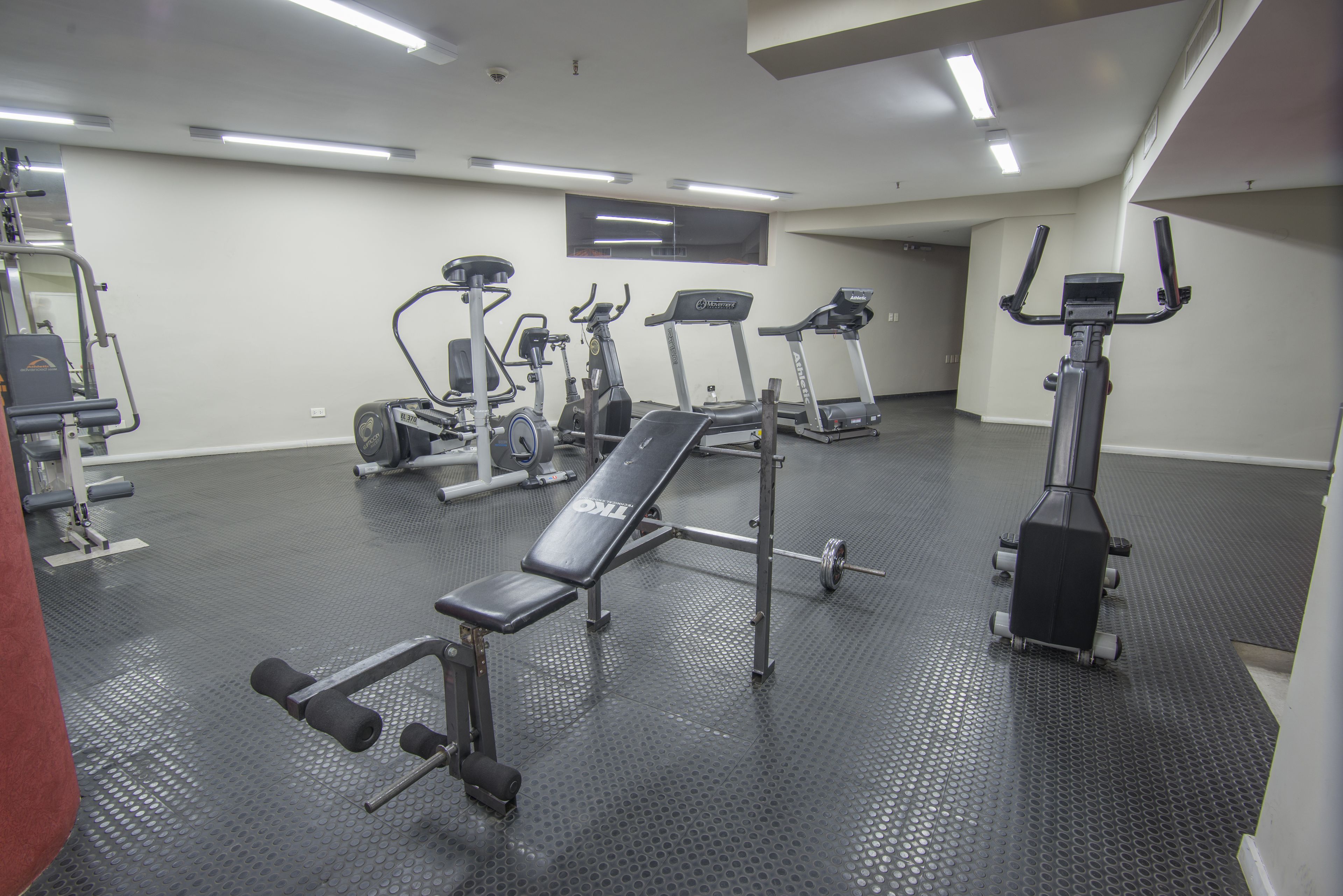 Un gimnasio con diversos equipos de ejercicio, incluyendo cintas de correr, una banca de pesas y máquinas de musculación.