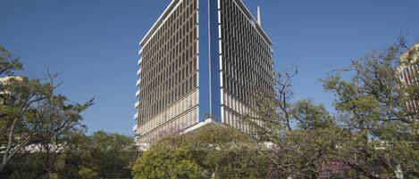 Un grand bâtiment moderne à la façade quadrillée, entouré d’arbres et de voitures garées.